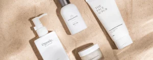 Verschiedene Hautpflegeprodukte auf sandigem Untergrund, darunter Sonnencreme, Gesichtspeeling und Feuchtigkeitscreme.