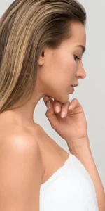 Profilansicht einer Frau mit langen, glatten Haaren, die eine weiße Handtuchumhüllung trägt und nachdenklich wirkt.